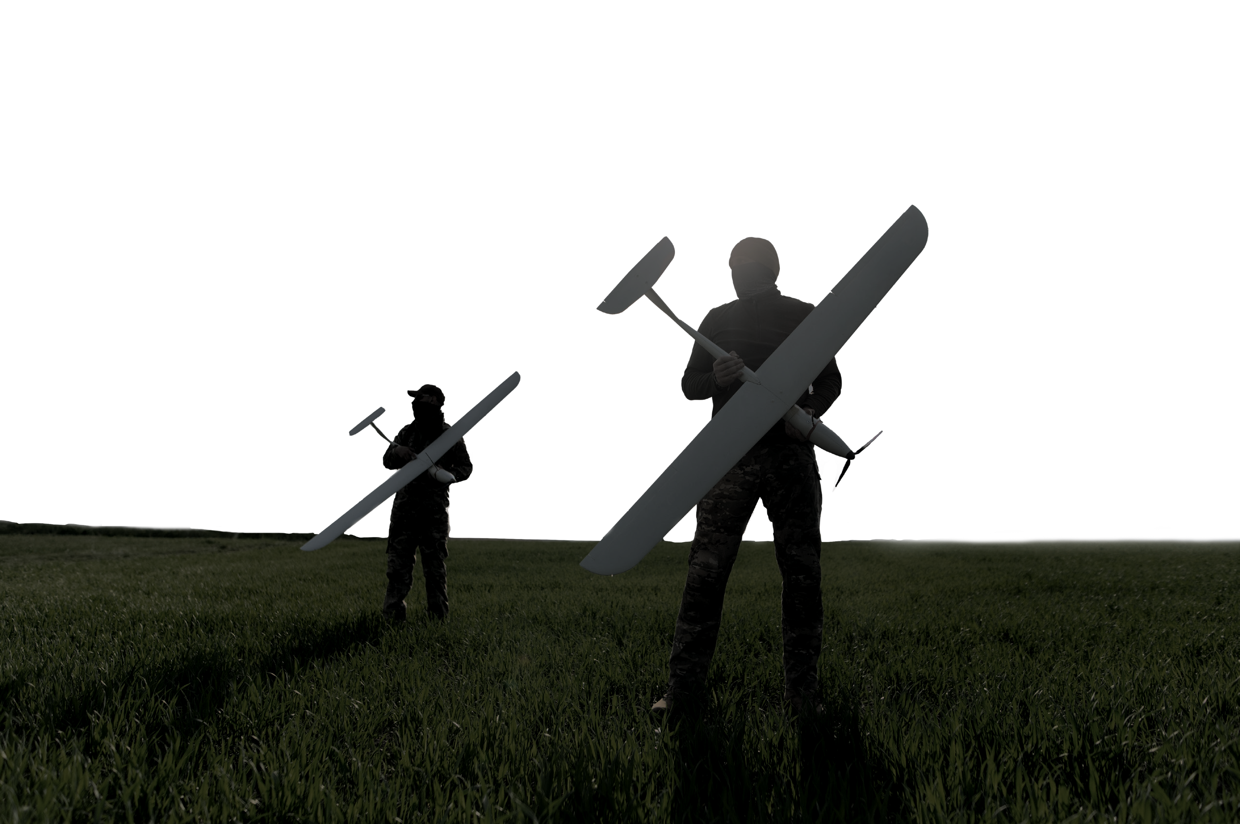 Two operators carrying fixed-wing unmanned aircraft across a field at dusk